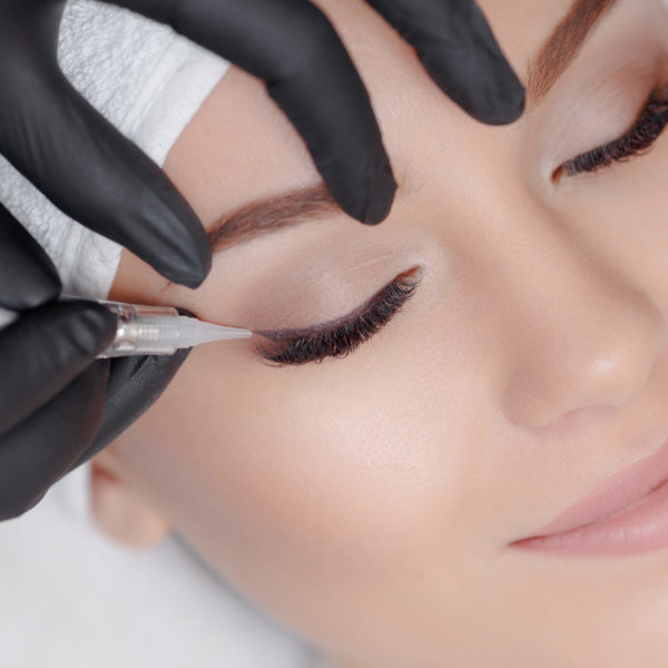 Cosmetologist making permanent makeup, close up. Tattooist making permanent make-up. Attractive lady getting facial care and tattoo. Permanent make-up tattoo at beauty salon