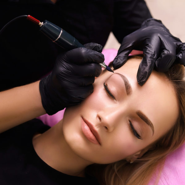 Cosmetologist applying permanent make up on eyebrows- eyebrow tattoo.