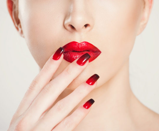 Make up and manicure set. macro cropped image of beautiful gradient of red black manicure and lipstick isolated on white background.