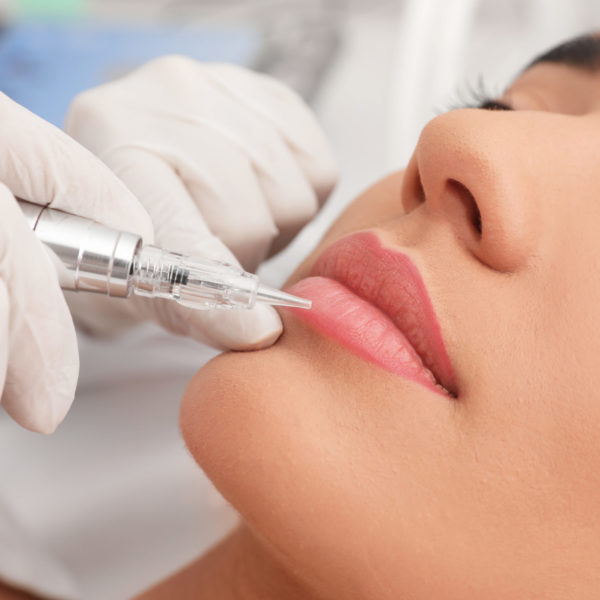 Young woman undergoing procedure of permanent lip makeup in tattoo salon, closeup